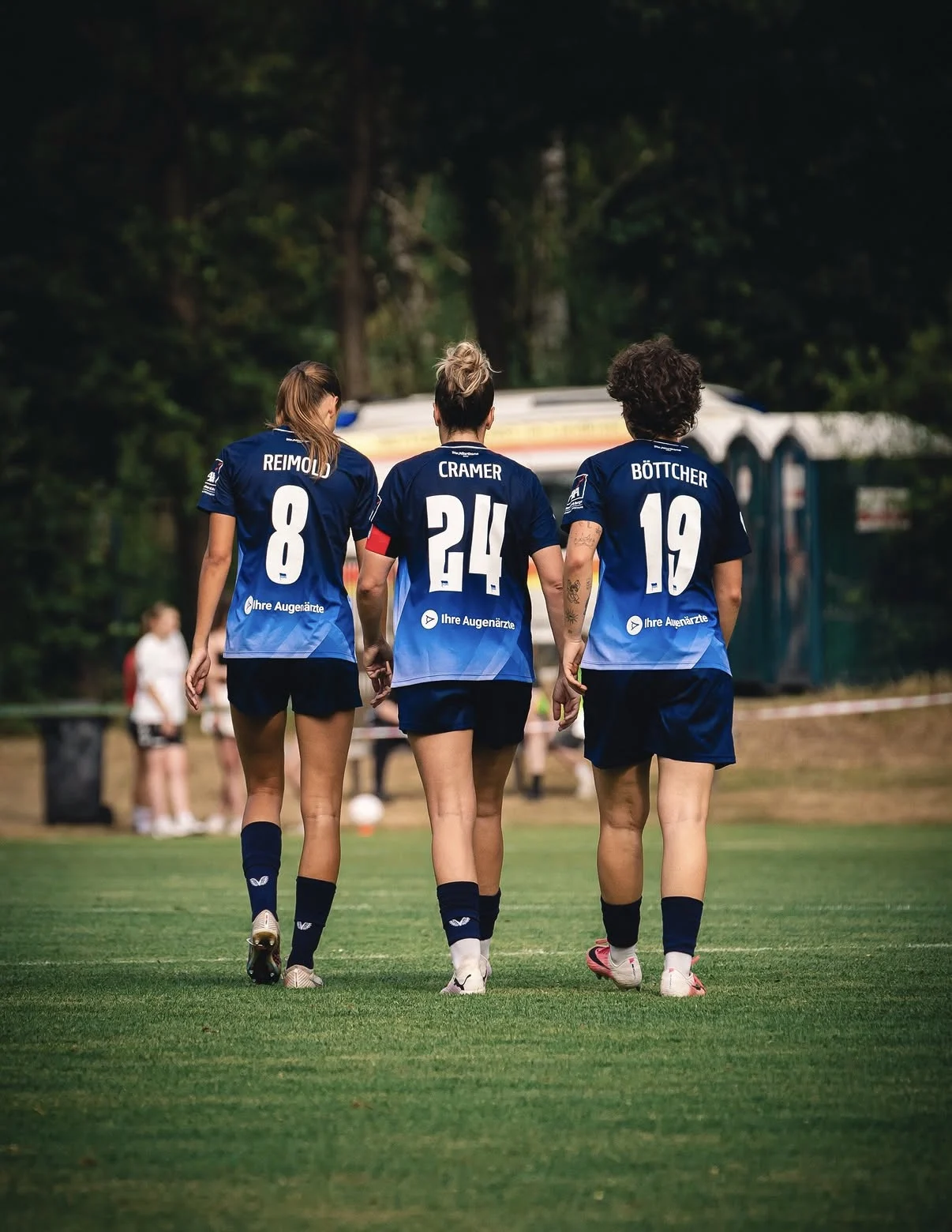 Drei Spielerinnen der Hertha BSC Frauen von hinten mit dem Logo von Ihre Augenärzte auf den Trikots